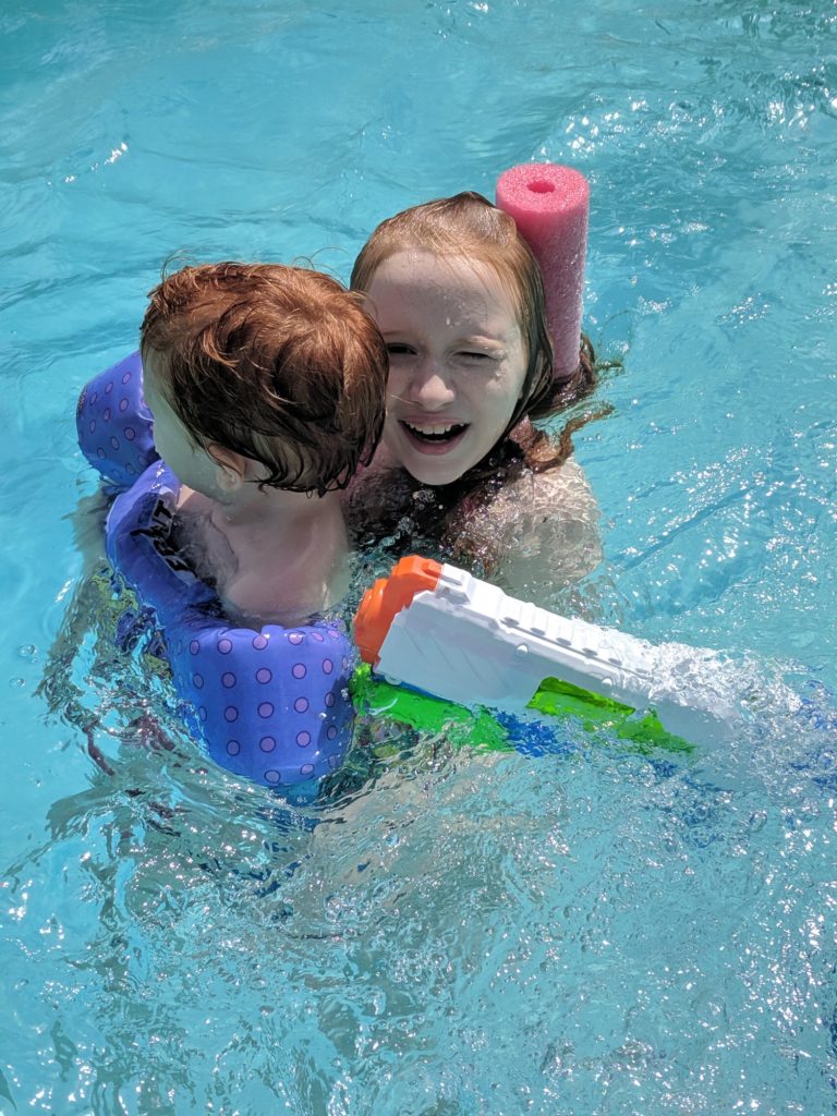 girl holding her little brother while swimming